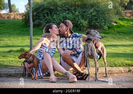 Jeune couple tatoué embrassant et embrassant, assis avec leurs chiens. Banque D'Images