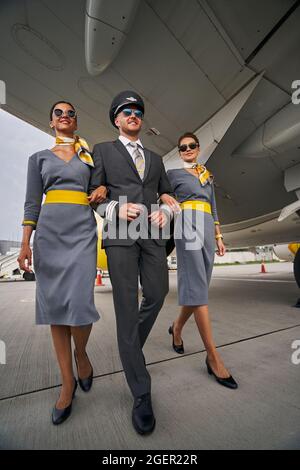 Un aviateur heureux accompagné d'hôtesses aux cheveux sombres va de l'avant Banque D'Images