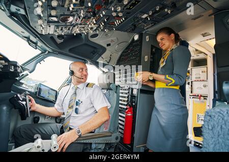 Le capitaine de la compagnie aérienne est heureux d'être servi un verre dans le poste de pilotage Banque D'Images
