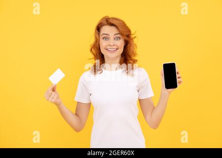 une jeune femme excitée a isolé un fond surjaune en utilisant un téléphone portable tenant une carte de crédit. Banque D'Images