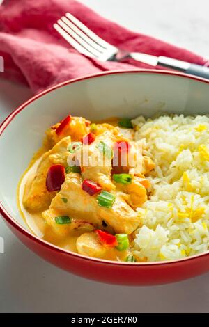 Curry de poulet thaïlandais au riz dans un bol rouge et blanc avec une serviette de table rose Banque D'Images