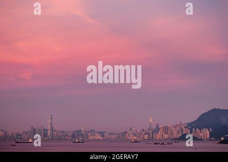 Kowloon, Victoria Harbour et l'horizon de l'île de Hong Kong avec les nuages roses de coucher de soleil reflétés dans l'eau du port Banque D'Images