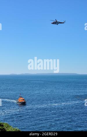 L'hélicoptère de sauvetage survole le canot de sauvetage de la classe Tamar de St David 16-26 'Norah Wortley' près de Porthclais avec Skomer Island au loin, Pembrokeshire Banque D'Images