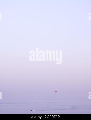 Vue minimaliste d'un parachute ascensionnel et d'un bateau sur la mer de Becici, au Monténégro, avec un ciel violet coloré et beaucoup d'espace de copie Banque D'Images