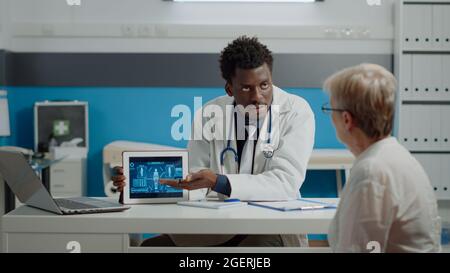 Un médecin professionnel expliquant l'animation de l'analyse du corps humain à une femme aînée dans un établissement médical. Médecin et patient âgé atteint d'une maladie en regardant l'analyse d'illustration sur un comprimé Banque D'Images