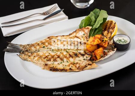 Bar de mer grillé et pommes de terre sur une assiette en porcelaine blanche. Banque D'Images