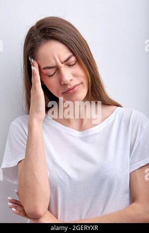 Belle femme caucasienne souffrant de maux de tête désespérés et stressés à cause de la douleur et de la migraine. Mains sur la tête. Jeune femme en t-s blanc décontracté Banque D'Images