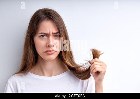 Contrarié femme frustrée tenant les cheveux dans les mains, veulent les couper, ayant des extrémités fractionnées, regarder la caméra avec une triste expression faciale. Femme caucasienne à ca Banque D'Images