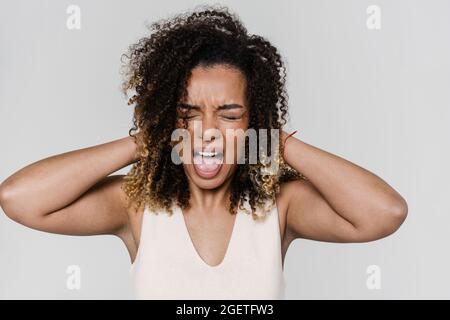 Le portrait d'une femme qui crie avec des yeux fermés couvrant les oreilles avec les paumes tout en se tenant dans le studio lumineux Banque D'Images