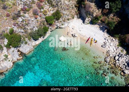 Vue aérienne époustouflante par drone de touristes faisant du kayak de mer dans une spectaculaire baie turquoise avec une plage de sable blanc le long de la côte sud de l'Albanie. Banque D'Images