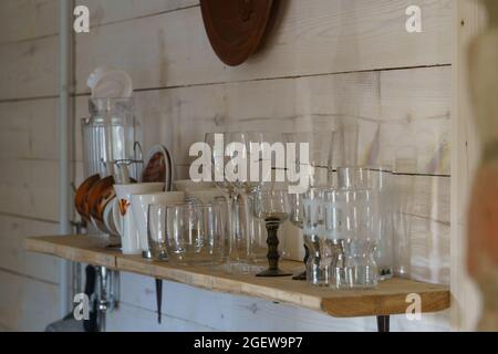 Mur de cuisine rustique avec étagère sur laquelle se trouve des verres à liqueur, des verres à vin, des verres à whisky, des verres à limonade et des tasses à café floues Banque D'Images