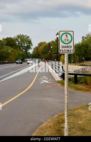 Ottawa (Ontario), Canada - le 20 août 2021 : des piétons et des cyclistes parcourent un sentier le long de la route Hog's Back, derrière un panneau « sentier rouge ». Banque D'Images