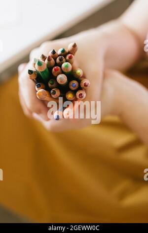 un tas de crayons de couleur dans les mains de la femme sur fond jaune, retour à l'école concept Banque D'Images