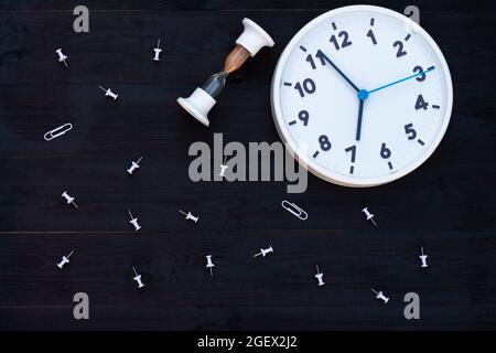 Horloge blanche, sablier et épingles sur fond en bois noir. Vue de dessus. Copier l'espace. Concept d'éducation ou d'entreprise. Banque D'Images