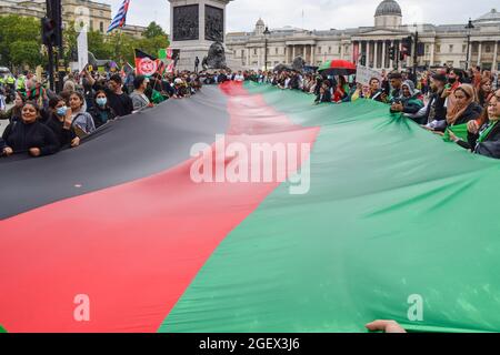 Londres, Royaume-Uni. 21 août 2021. Les manifestants détiennent un drapeau géant de l'Afghanistan pendant la manifestation à Trafalgar Square. Des manifestants ont défilé dans le centre de Londres pour protester contre la prise de pouvoir par les talibans de l'Afghanistan et ont appelé le gouvernement britannique à imposer des sanctions au Pakistan et à aider le peuple afghan. Crédit : SOPA Images Limited/Alamy Live News Banque D'Images