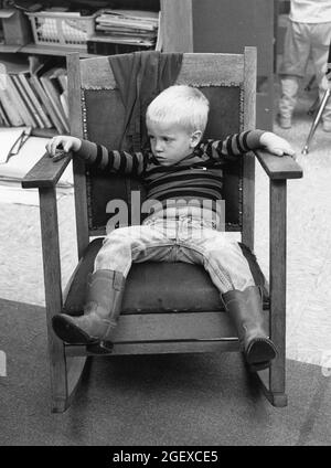 Austin Texas USA, vers 1993: Pré-école garçon portant des bottes de cowboy faisant le temps dehors dans la chaise dans la salle de classe de garderie. ©Bob Daemmrich Banque D'Images