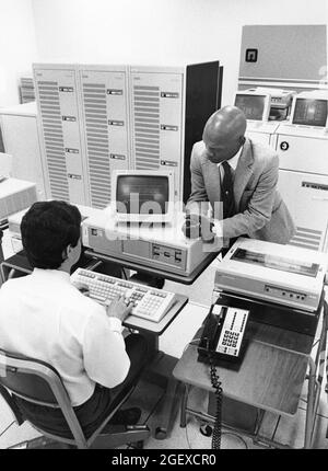 Austin Texas USA,1990: Le superviseur regarde le travail de spécialiste de la saisie de données sur le terminal informatique avec ordinateurs mainframe en arrière-plan à un traitement c Banque D'Images