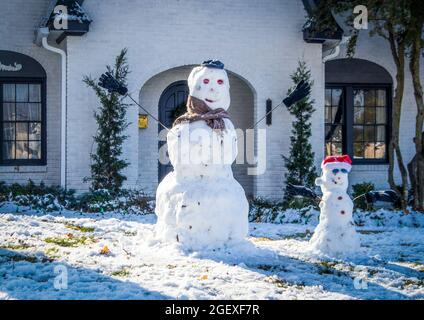 Deux bonhommes de neige mignons devant une maison en briques peintes en blanc - un grand avec foulard et un petit avec chapeau de père noël Banque D'Images