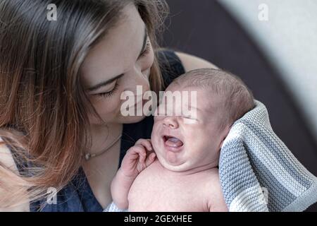 Une jeune mère tient un nouveau-né pleurant dans les bras, gros plan. Banque D'Images