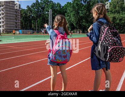 Les petites filles écoliers avec des sacs à dos dans le stade, en regardant les garçons jouer au football. Banque D'Images