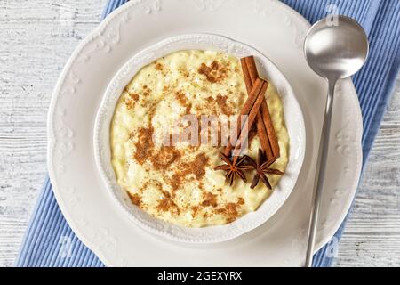 pudding de riz à la cannelle et étoile anisée dans un bol blanc avec une cuillère sur une table en bois blanc Banque D'Images