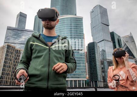 Moscou, Russie. 21 août 2021 UN jeune couple portant des lunettes de réalité virtuelle est photographié au festival de technologie de la science de pique-nique de Geek, dans le contexte des gratte-ciels du centre financier et de bureau 'Moscow City' à Moscou, en Russie Banque D'Images