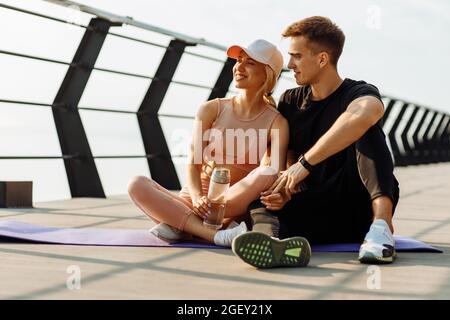 Un couple en bonne santé se reposant après une séance d'entraînement à l'extérieur, un couple s'exerçant ensemble, un homme et une femme se reposant après un cours de fitness sur un tapis de fitness sur la jetée Banque D'Images