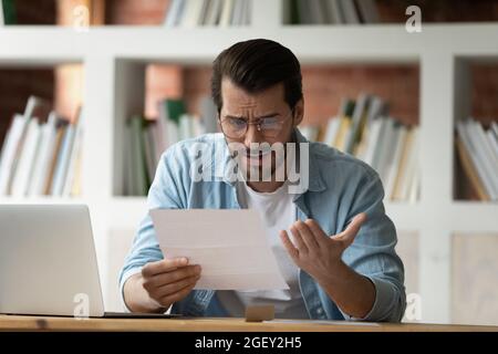 Un jeune homme tenant une lettre en papier lisant des nouvelles inattendues choquantes Banque D'Images