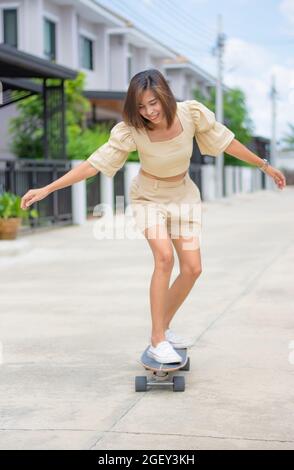 Femme asiatique debout sur Surfskate arrière-plan des rues et des maisons. Banque D'Images
