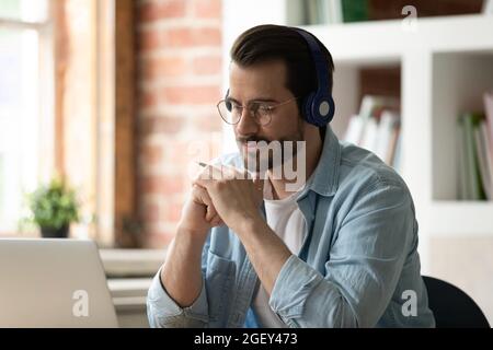 Un homme attentif utilise un ordinateur portable pour écouter le cours audio à l'aide d'un casque Banque D'Images