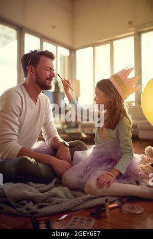 Une petite fille aime mettre le maquillage sur le visage de son père lorsqu'ils se préparent à des exercices de ballet dans une atmosphère détendue à la maison. Famille, ensemble, Banque D'Images