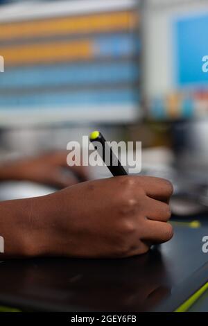 Gros plan de l'image client de l'édition de concepteur noir avec un crayon de stylet, dessin sur une tablette graphique. Main de femme afro-américaine rédactrice photographe retouche des actifs travaillant dans le bureau de la société de production créative Banque D'Images