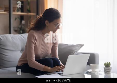 Une femme sérieuse et concentrée porte des lunettes qui travaillent sur un ordinateur portable Banque D'Images