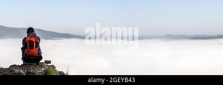 une femme voyageur dans les montagnes se trouve au bord d'une falaise et admire un matin brumeux dans les montagnes, une vue de l'arrière. l'aube sur les collines Banque D'Images