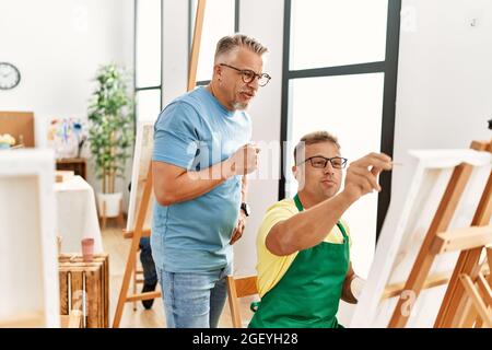 Groupe d'étudiants en peinture d'âge moyen qui dessinant au studio d'art. Professeur avec l'expression sérieuse regardant le dessin étudiant. Banque D'Images