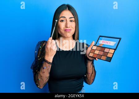 Jeune femme hispanique tenant la brosse à maquillage et rougir puffant les joues avec le visage drôle. Bouche gonflée avec de l'air, attrapant l'air. Banque D'Images