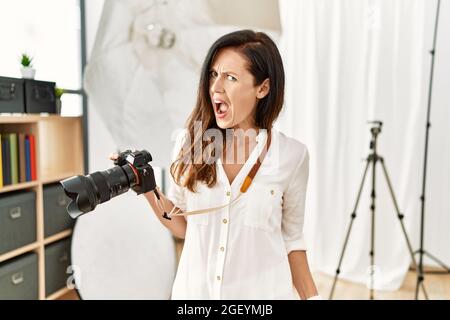 Belle femme caucasienne travaillant comme photographe au studio de photographie en colère et fou criant frustré et furieux, criant avec colère. Rage et Banque D'Images