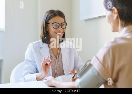 Jeune femme africaine positive médecin montrant le signe ok tout en vérifiant la tension artérielle de la patiente Banque D'Images