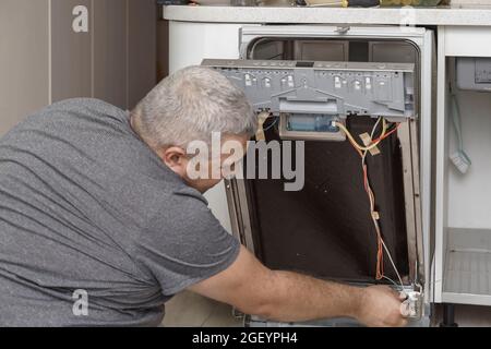 Personnel dans les emplois de technicien. Un technicien de réparation d'appareil travaille sur un lave-vaisselle cassé dans un kittchen. Banque D'Images