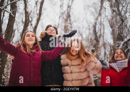 Groupe de quatre meilleurs amis joyeux qui profitent du temps froid et de la première neige en plein air sur des arbres couverts de neige, levant les mains et essayant d'attraper Banque D'Images