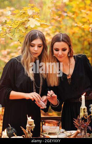 Jeunes femmes en costumes de sorcière assis à table avec des ingrédients magiques le jour d'automne dans la forêt Banque D'Images