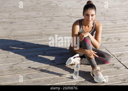 Image d'une jeune athlète féminine attrayante ayant une pause après l'entraînement, assis sur une jetée en bois et profitant de la vue sur la mer Banque D'Images