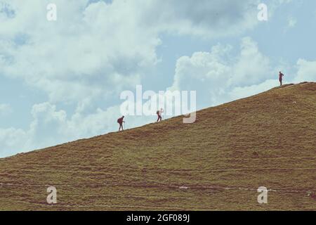 Homme et femme grimpant sur une colline. Leur ami les attend au sommet. Randonnée en montagne. Concept de travail d'équipe. Expérience de motivation Banque D'Images