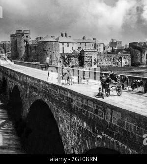 Une vue du début du XXe siècle sur les véhicules tirés par des chevaux et les gens sur le pont Thormond au-dessus de la rivière Shannon surplombé par le château du roi John du XIIIe siècle, ville de Limerick, Irlande Banque D'Images