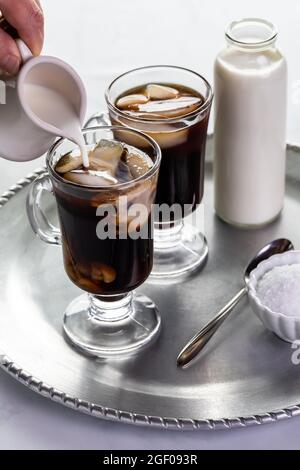 versez à la main la crème dans une boisson glacée au café avec une bouteille de lait dans un plateau métallique Banque D'Images