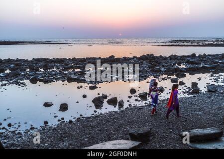 Mumbai, Maharashtra, Inde : deux jeunes femmes marchent au coucher du soleil sur le sol à marée basse par la chaussée menant au pèlerin Haji Ali Dargah du XIXe siècle Banque D'Images