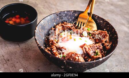 Porc coréen avec œuf sur riz dans un bol plaque en céramique avec cuillère en métal et fourchette. Un plateau traditionnel coréen repas cuisine. Banque D'Images