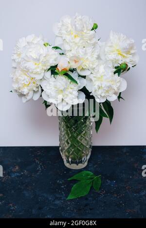 Magnifique bouquet de fleurs de pivoine blanches avec gouttes d'eau sur les pétales dans un vase en verre sur une table Banque D'Images