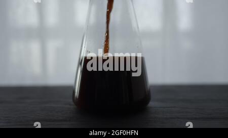 le café froid s'écoule dans une carafe en verre sur une table en chêne noir, photo large Banque D'Images
