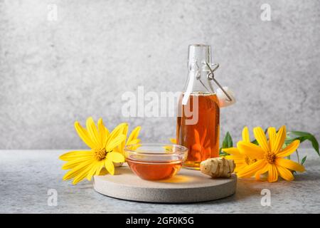 Sirop d'artichaut Jérusalem en bouteille, fleurs et racine sur fond gris. Copier l'espace. Banque D'Images